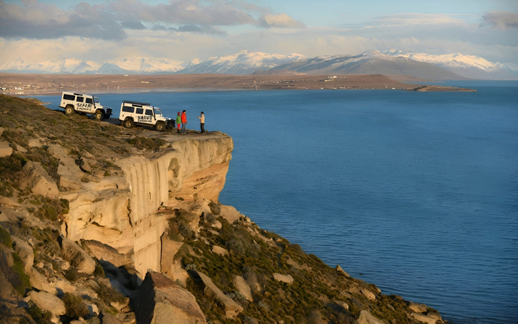 Two 4x4 vehicles parked at the edge of a sandstone cliff above the blue water of Lago Argentino