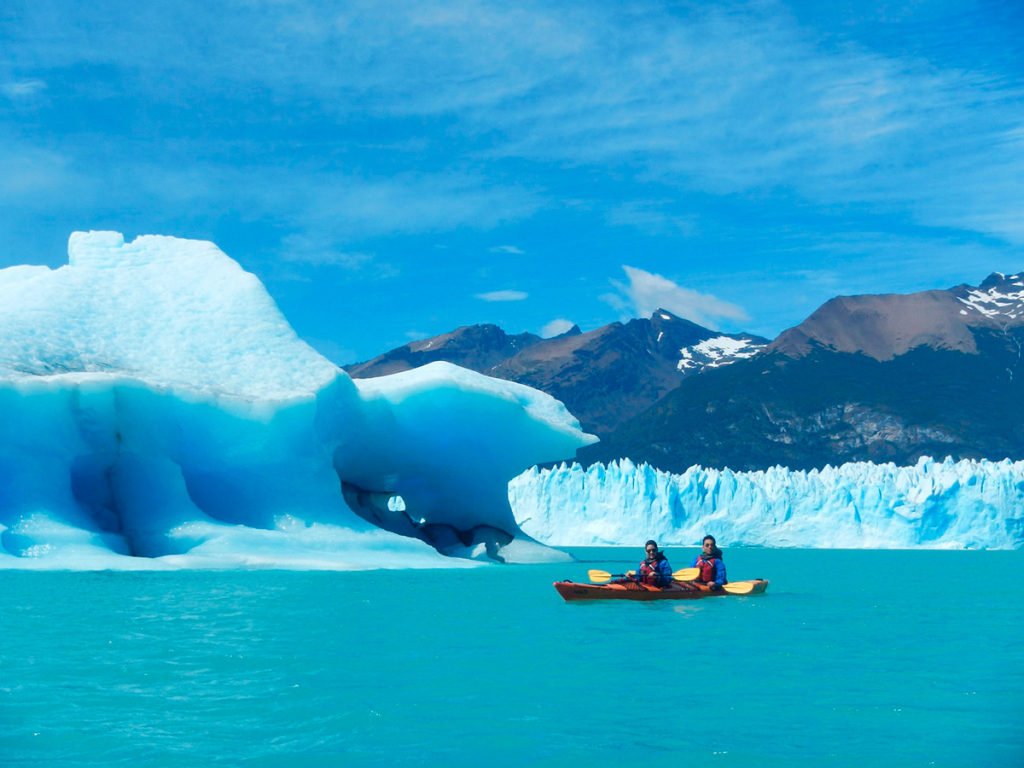 A single sea kayak dwarfed by icebergs and the glacier front on the turquoise water of Lago Argentino