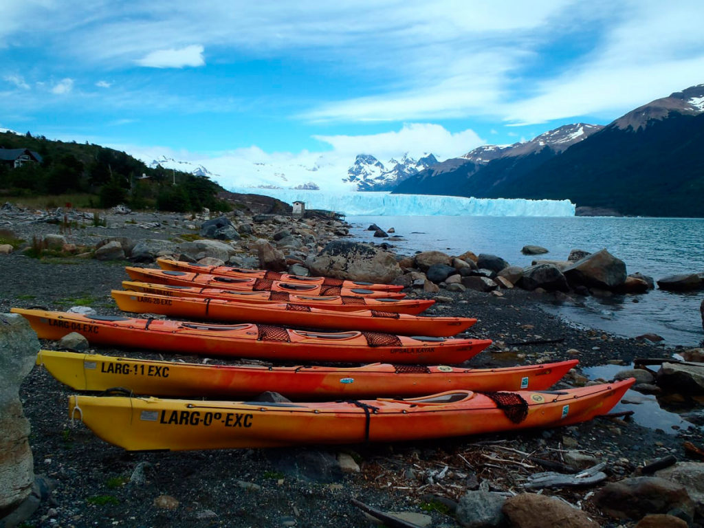Row of sea kayaks lined up on the stony shore of Lago Argentino with the glacier beyond