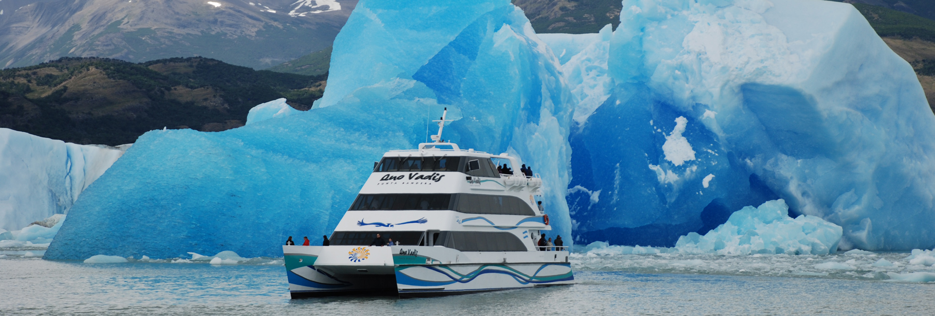A boat passing a huge blue iceberg on Lago Argentino, in Los Glaciares National Park