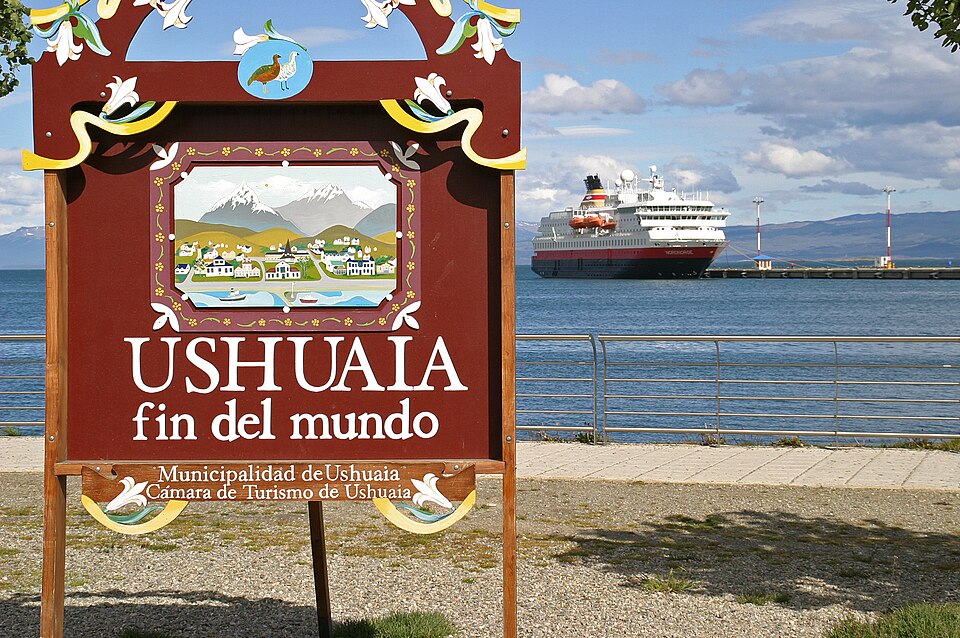 The carved wooden Ushuaia sign reading fin del mundo, with a ship in the bay behind