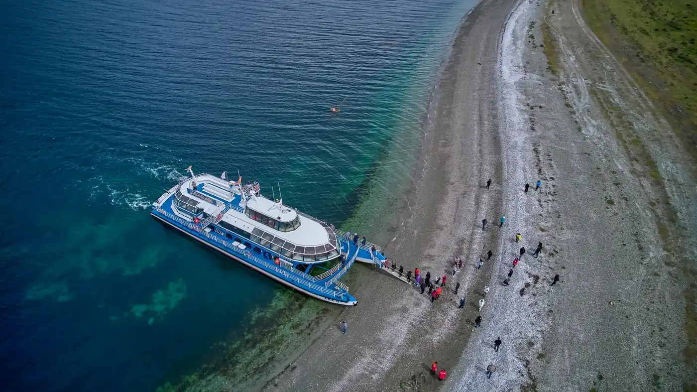 Aerial view of the catamaran beached on the gravel shore with passengers walking ashore near Puerto Almanza