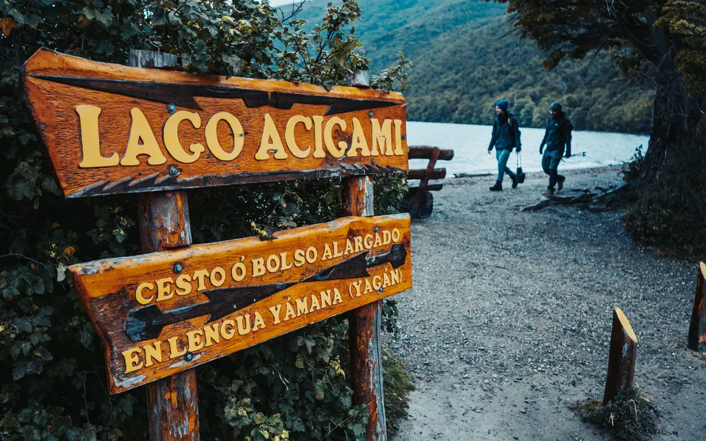 Two walkers heading to the shore of Lake Acigami past the carved wooden sign, Tierra del Fuego National Park