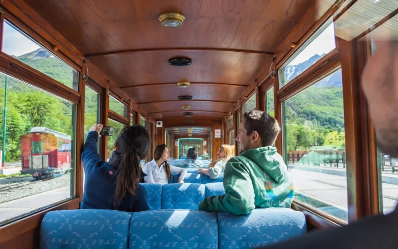 Passengers inside a heated carriage of the End of the World Train, with large windows onto the forest