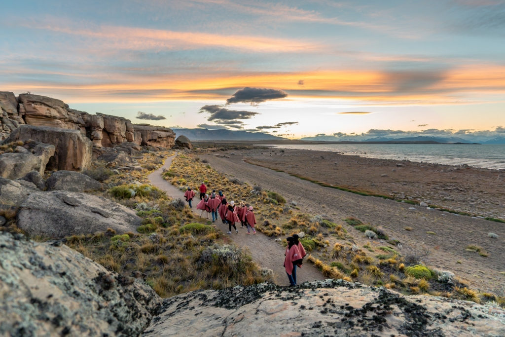 Group in red jackets walking down a path to the shore of Lago Argentino under a pink sunset sky